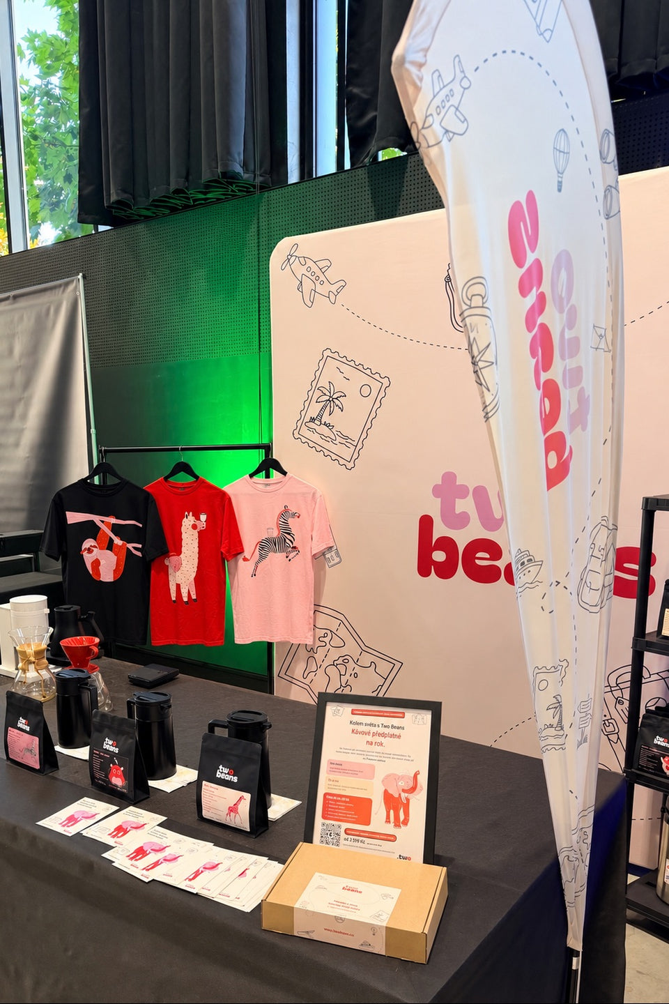 Stánek two beans na Prague Coffee Festivalu 2026: trička, káva a plakát s předplatným